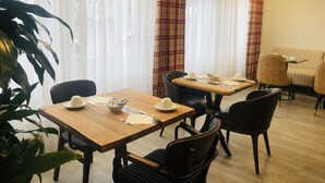 Een eetgedeelte met een houten tafel en stoelen, een kommetje met bestek en een gedekte tafel met bekers en een schaal.