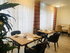 Un coin repas avec une table et des chaises en bois, un récipient contenant des ustensiles et une table dressée avec des tasses et un bol.