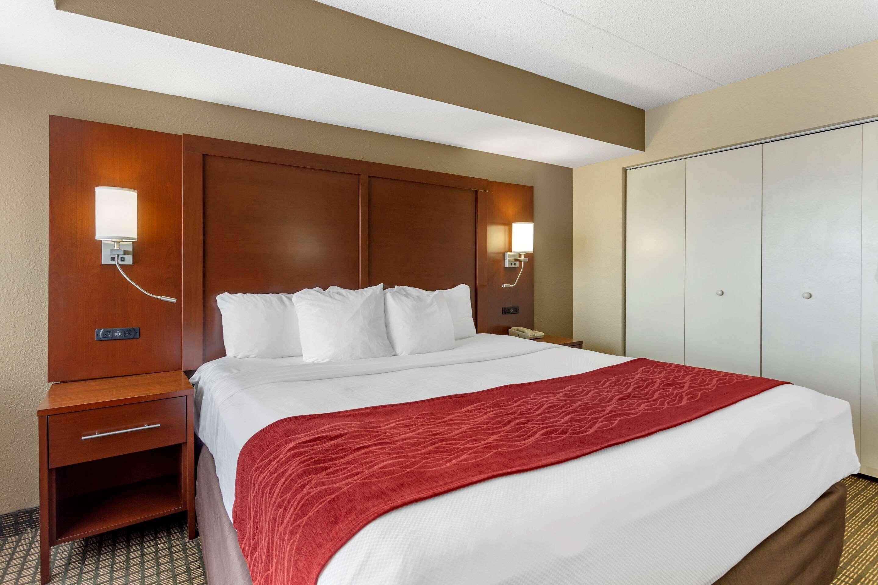 A hotel room with a large bed, wooden headboard, bedside lamps, a nightstand, and a wardrobe.