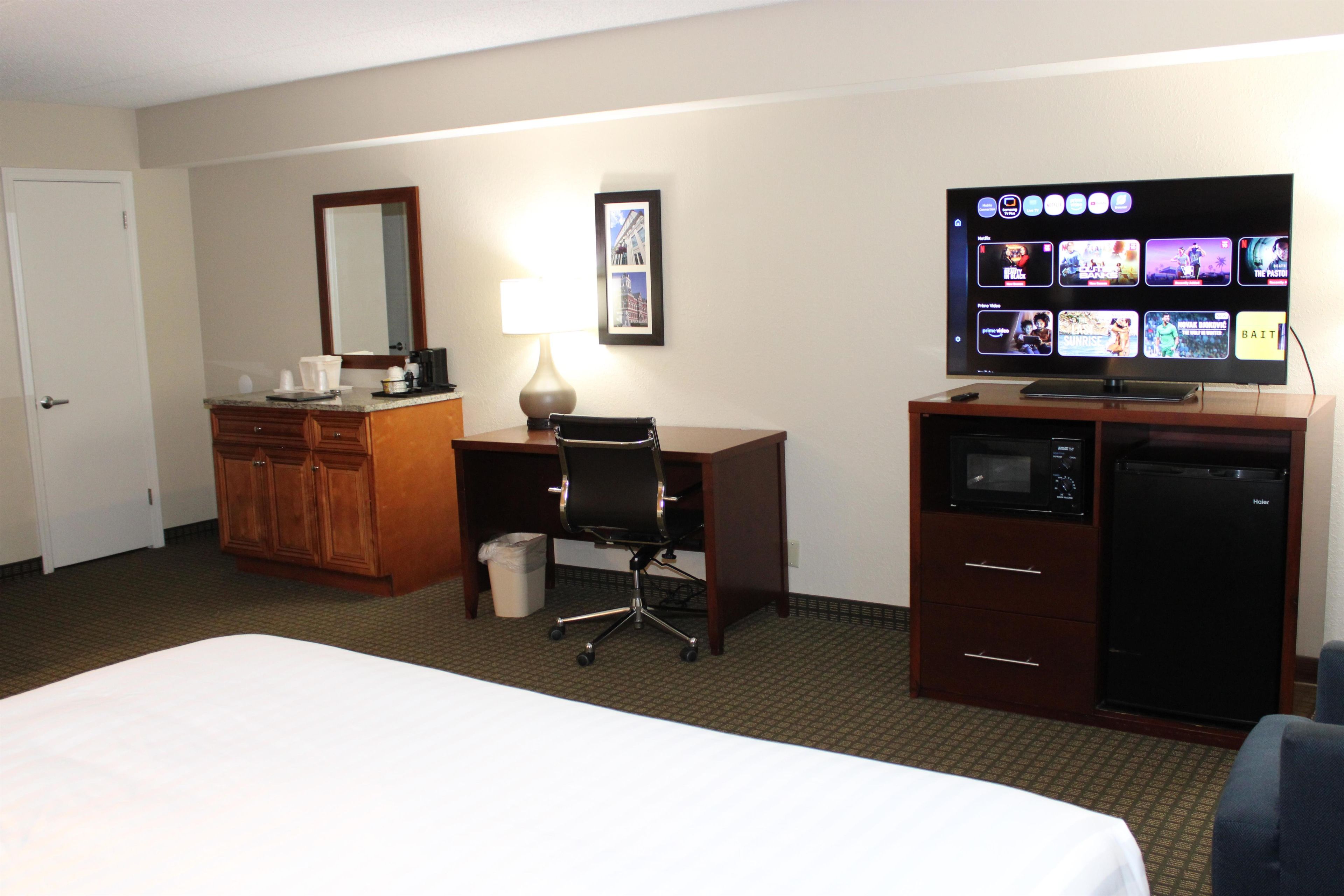 Una habitación de hotel con una cama, un escritorio, un televisor, un microondas y un refrigerador.