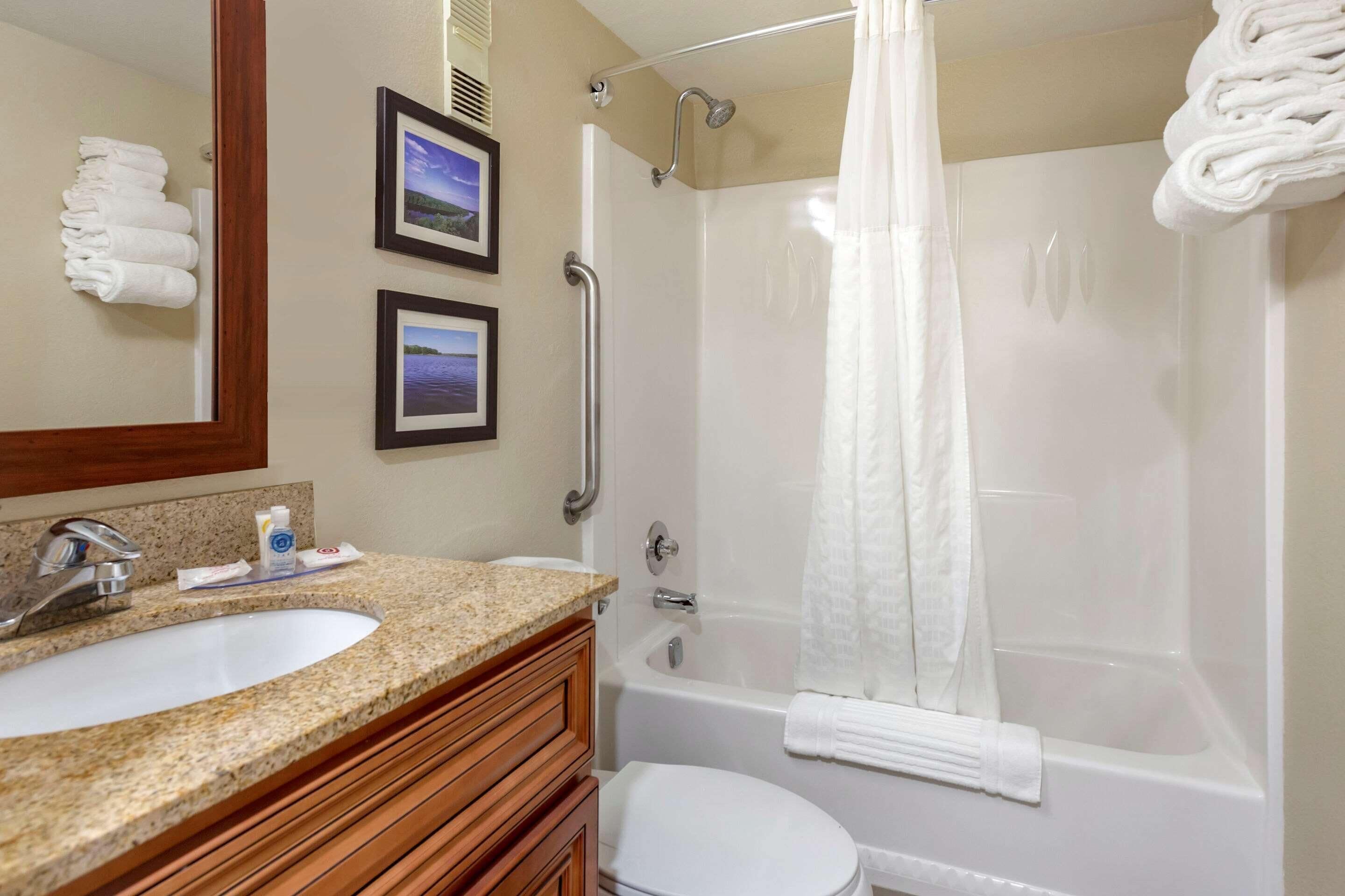 A bathroom with a sink, toilet, and shower. There are towels stacked on the wall and a framed picture.