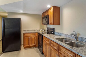 Una cocina con armarios de madera, un refrigerador negro, un microondas, un horno y una encimera de granito con un lavamanos.