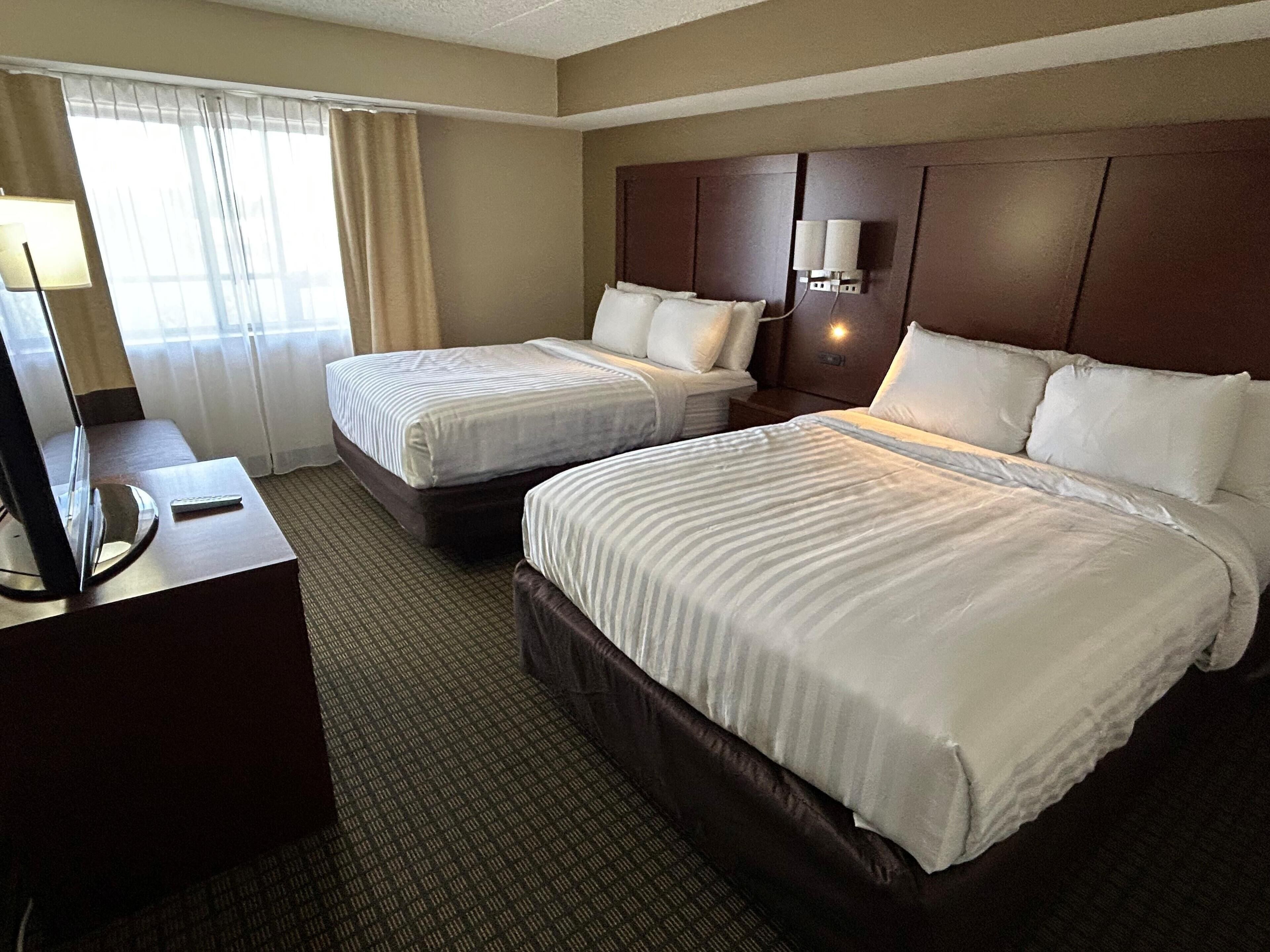 A hotel room with two beds, a desk with a lamp, and a window with curtains.