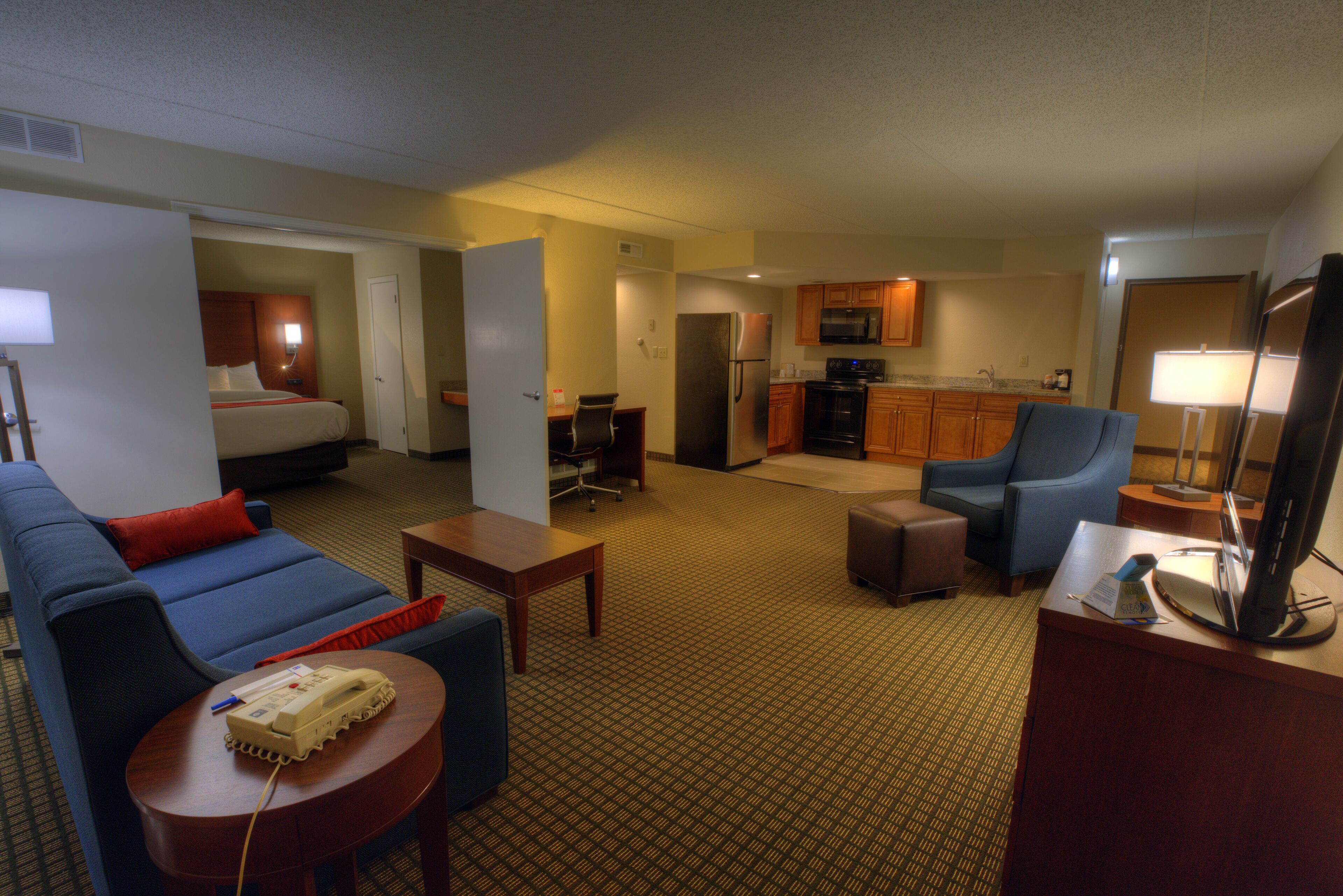 A hotel room with a living area, kitchenette, and a bed.