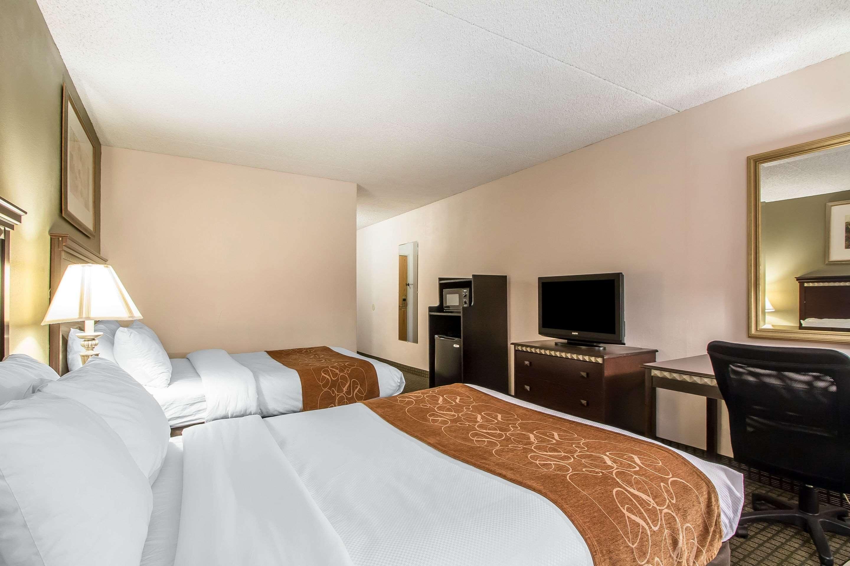 A hotel room with two beds, a desk, a chair, a television, and a mirror.