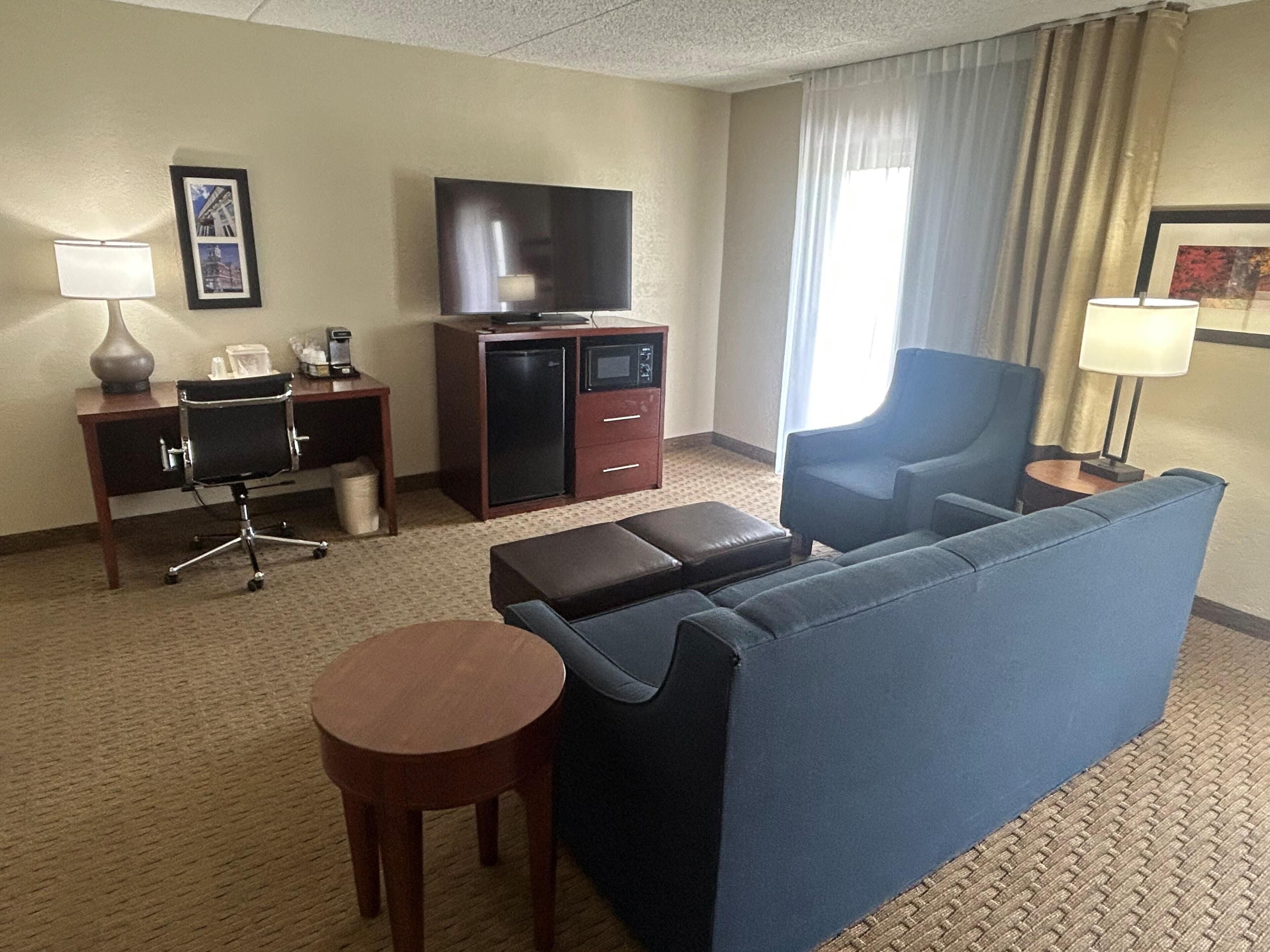 Een hotelkamer met een bank, een klein tafeltje, een bureau met lamp, een televisie en een minibars.