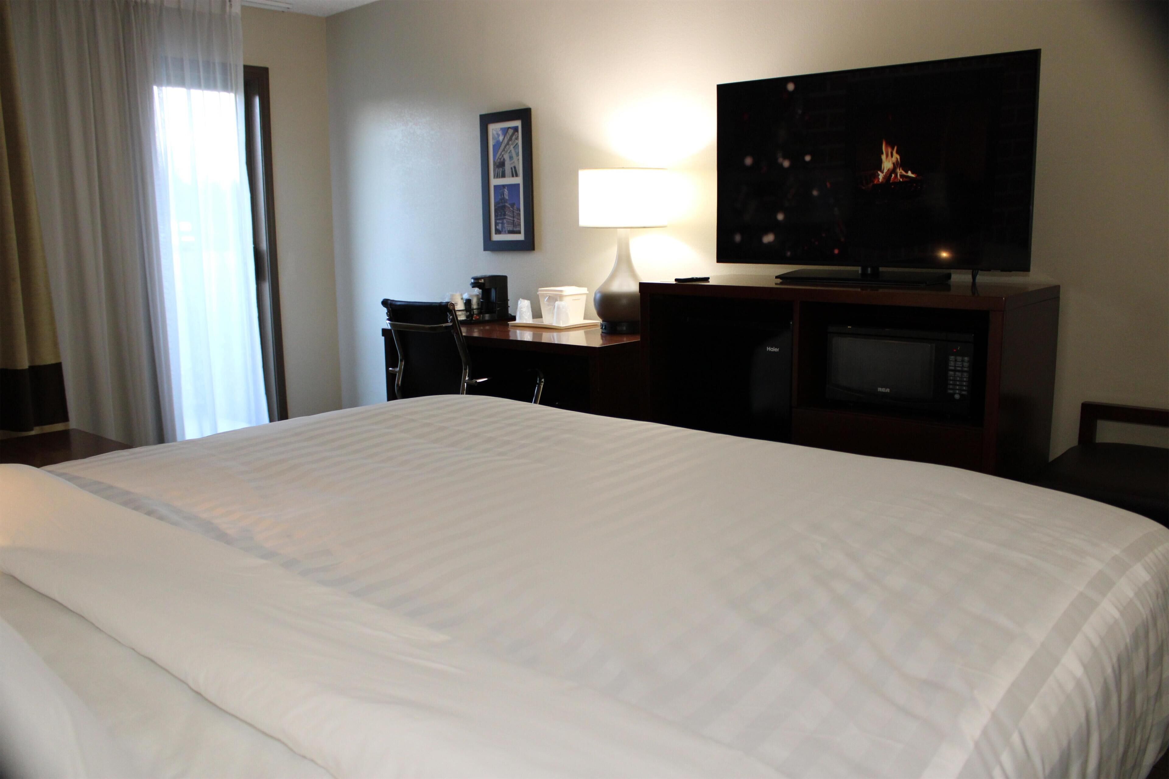 Una habitación de hotel con una cama grande, un escritorio con ordenador, televisión y microondas.