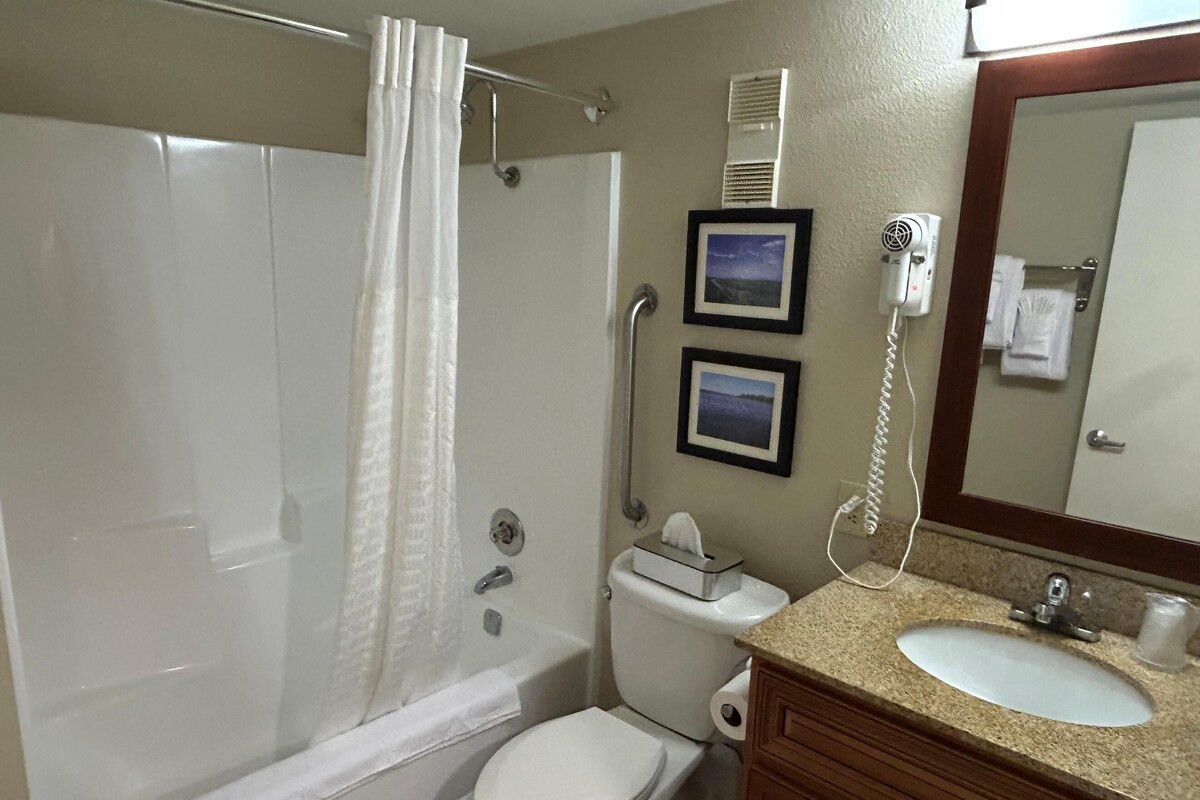 A bathroom with a shower, toilet, sink, and a mirror with a towel hanging.
