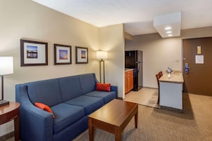 Habitación de hotel con sofá, una mesita, lámpara, kitchenette y cuadros en la pared.