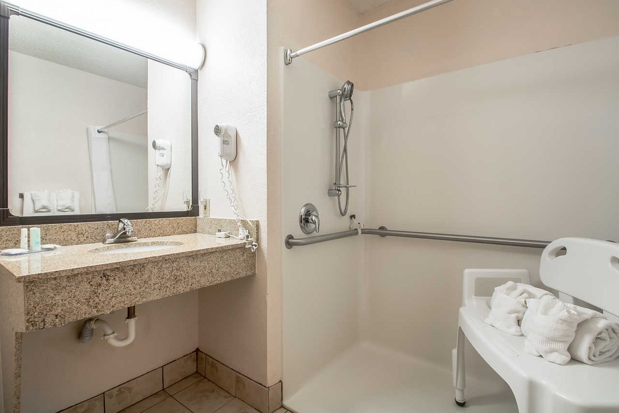 A bathroom with a sink, mirror, towel rack, shower, and grab bar.