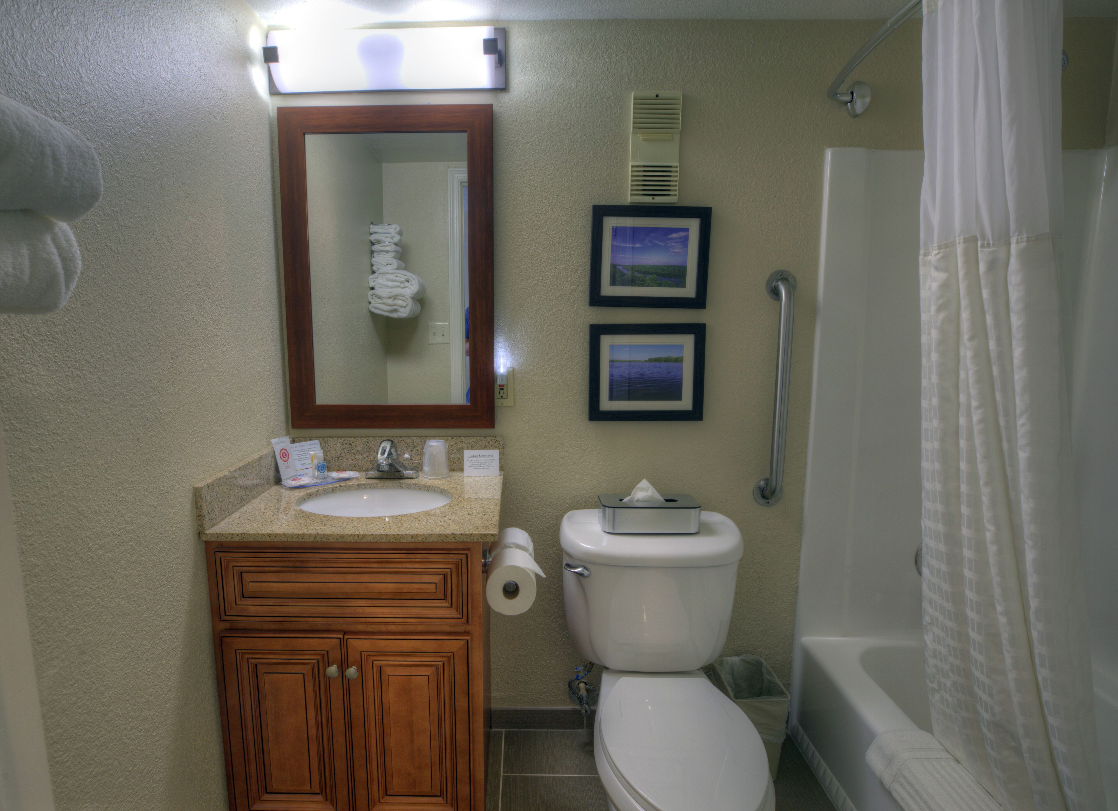 A bathroom with a sink, toilet, and shower. There are framed pictures on the wall and a handrail next to the shower.