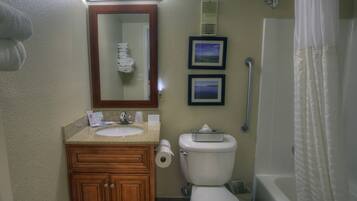 A bathroom with a sink, toilet, and shower. There are framed pictures on the wall and a handrail next to the shower.