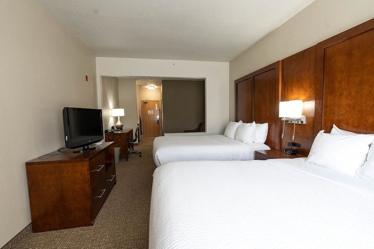 A hotel room with two beds, a TV, a desk, and a lamp.