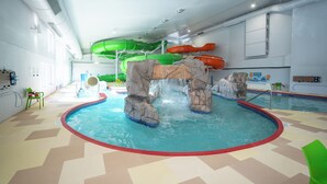 Une piscine intérieure dotée de toboggans, d’une structure rocheuse et d’un sol à motifs en chevrons.