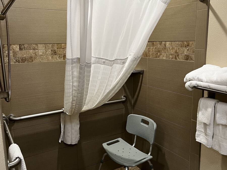 A bathroom with a shower, a grab bar, a wheelchair-accessible chair, and a towel rack.