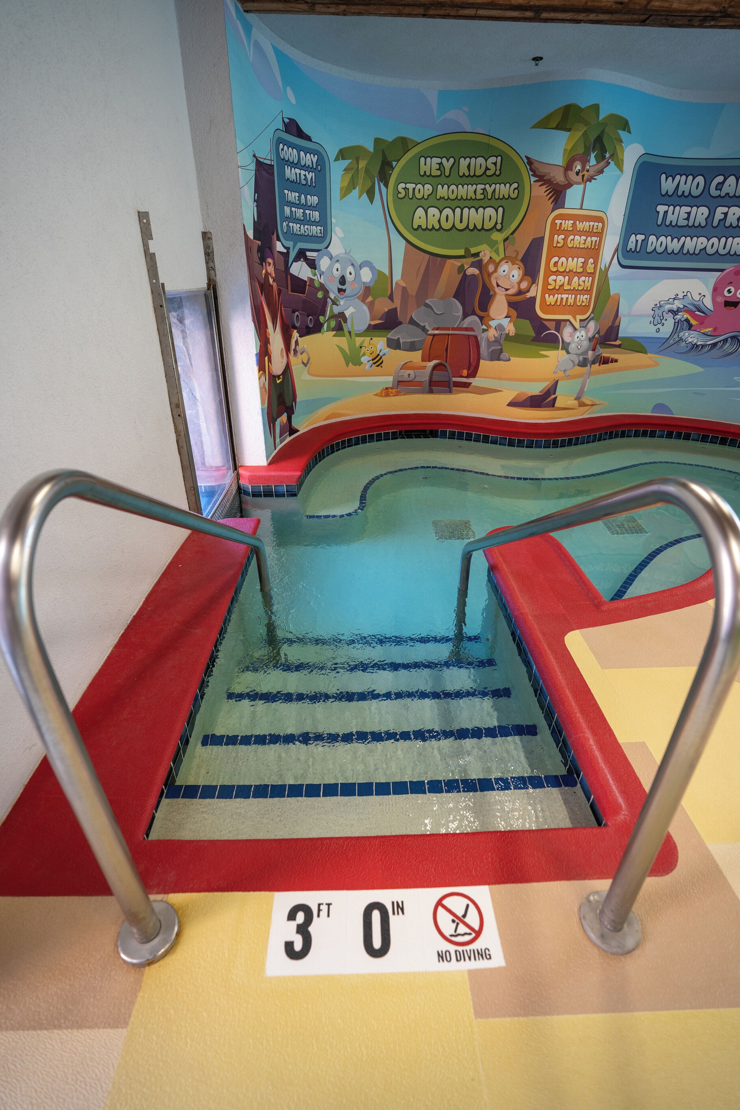 A pool with a no diving sign, a 3ft 0in depth marker, and a mural with cartoon characters.