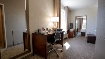 A hotel room with a desk, chair, lamp, television, and a large mirror.