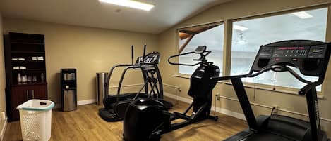 Ett hemmagym med löpband, crosstrainer och motionscykel, trägolv och ett stort fönster med utsikt.