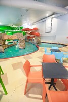 Un área de piscina interior con toboganes, mesas y sillas.