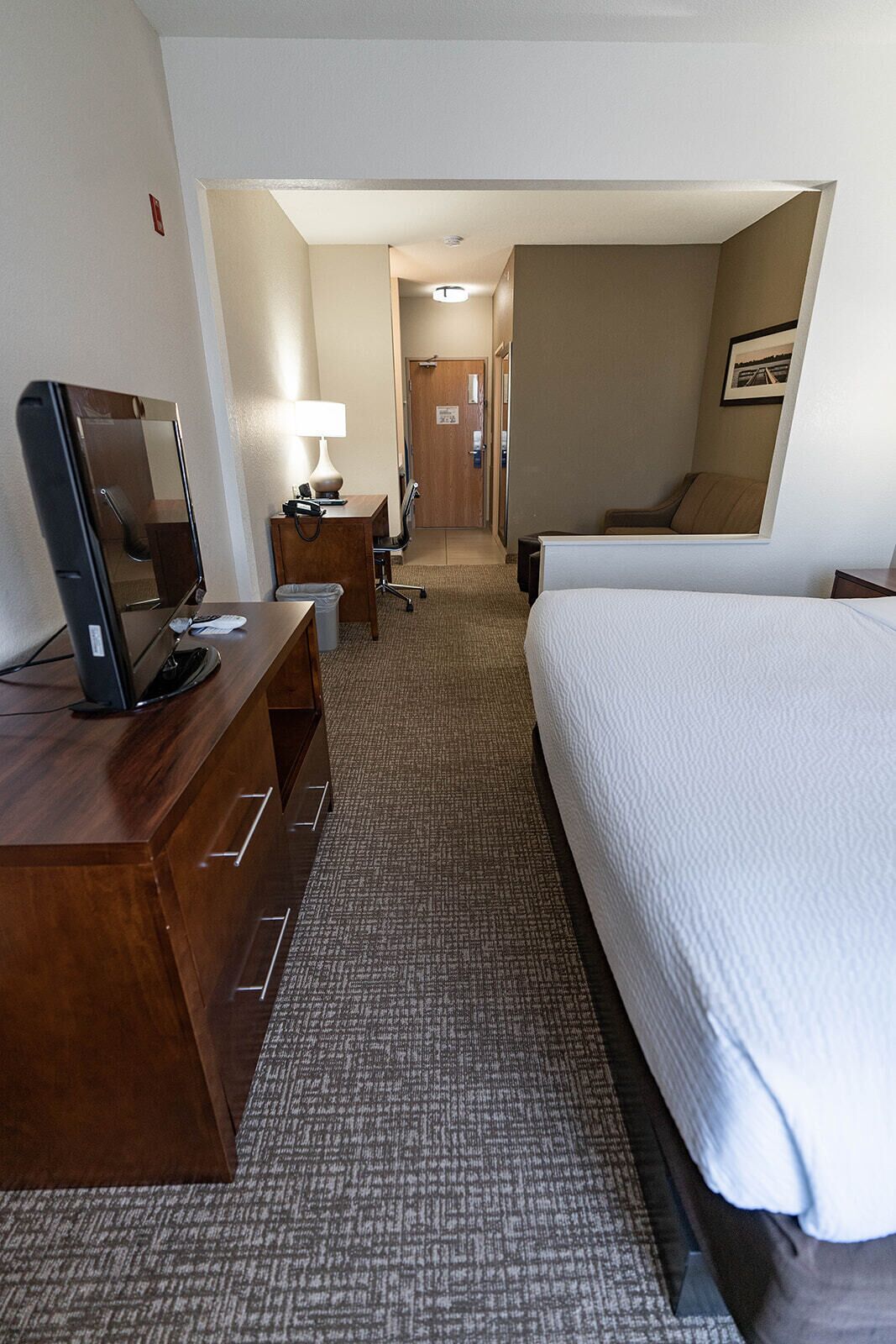 A hotel room with a bed, a desk with a computer, a lamp, and a television.