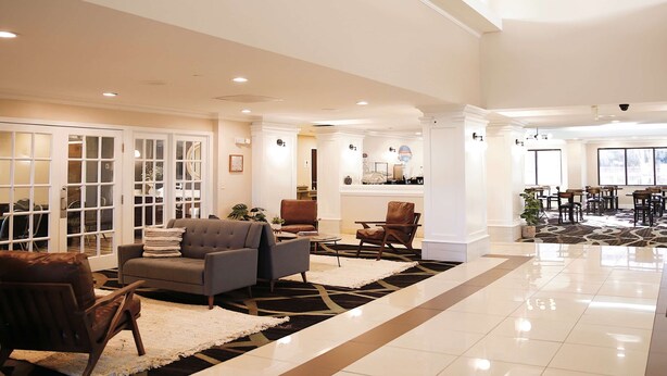 A spacious lobby with a modern design, featuring a seating area with sofas and chairs, a kitchen area, and a dining space with tables and chairs.