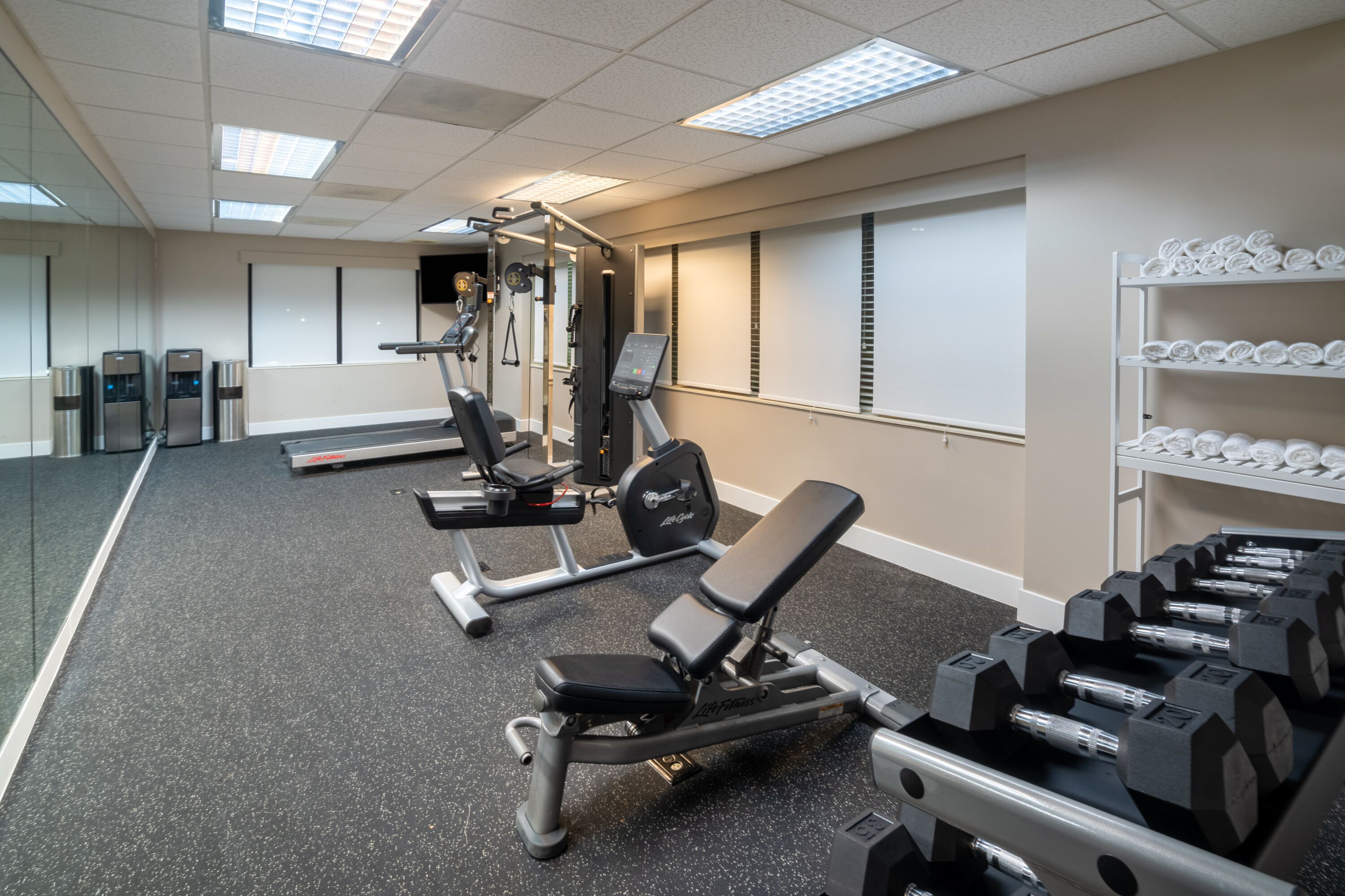 A gym with exercise equipment, a water dispenser, and a shelf with towels.