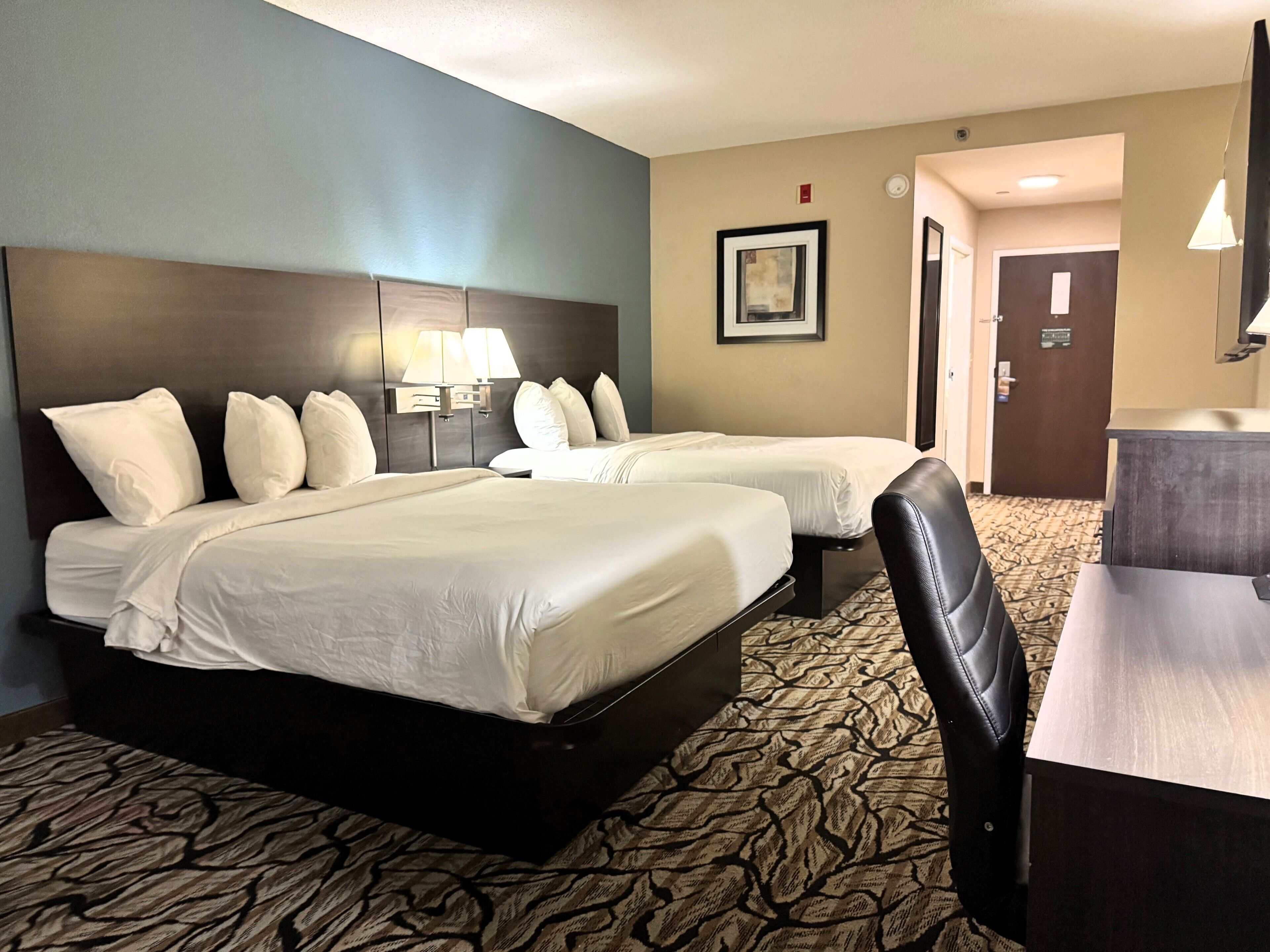 A hotel room with two beds, a desk, and a chair.