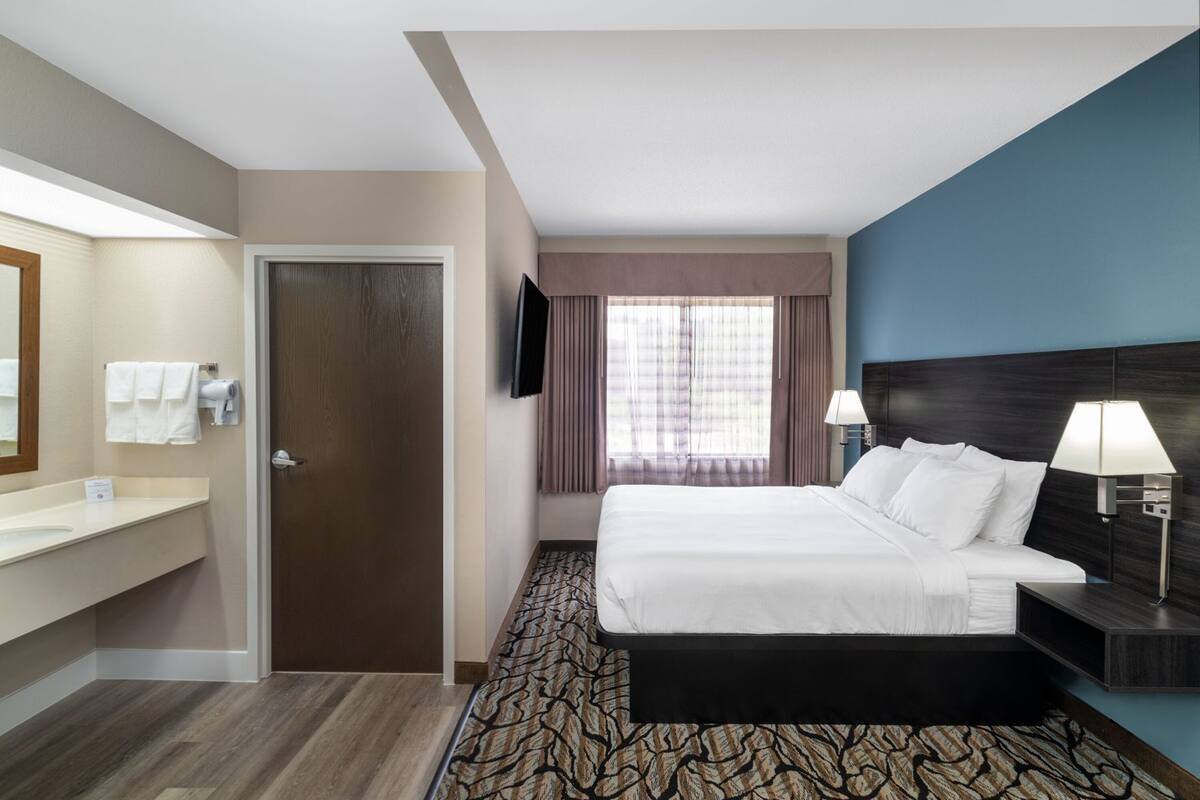 Une chambre d’hôtel avec un lit, une télévision, une salle de bain avec un miroir et une fenêtre avec des rideaux.