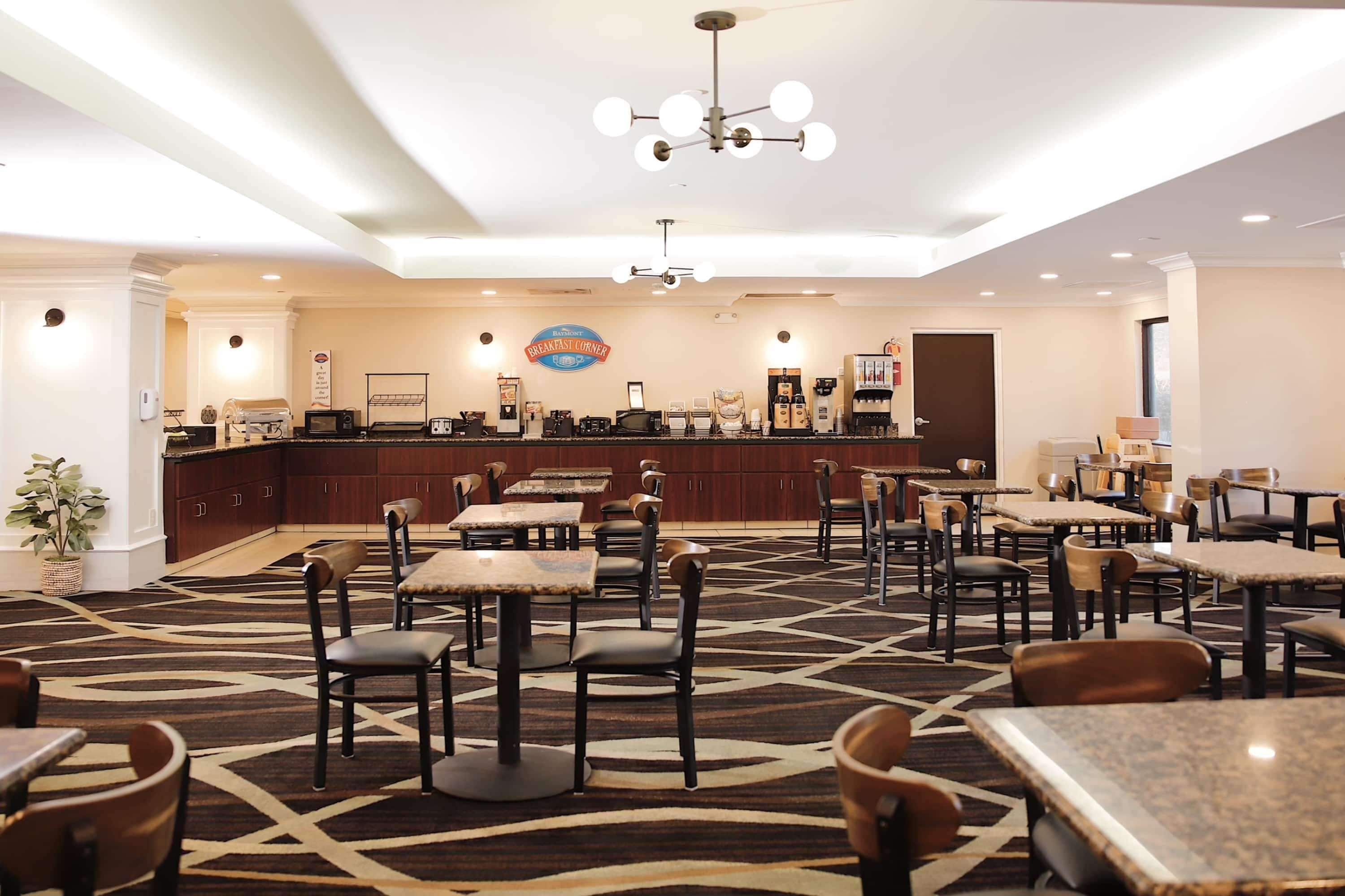 A restaurant with a patterned carpet, multiple tables and chairs, a bar area, and a ceiling light fixture.