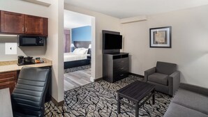 A hotel room with a bed, a TV, a desk with a microwave, a chair, and a sofa.