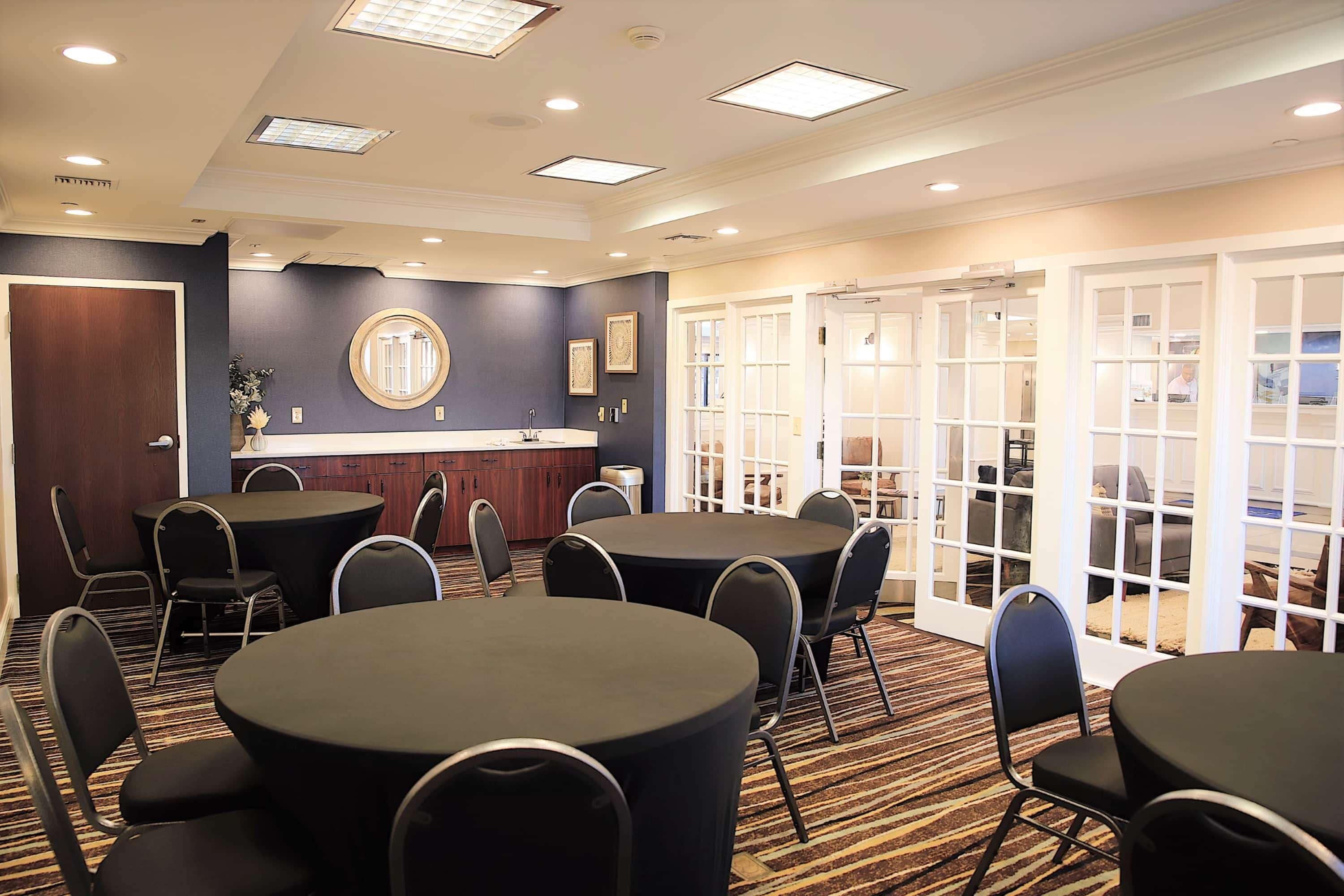 A conference room with round tables and chairs, a reception desk, and a view through glass doors.