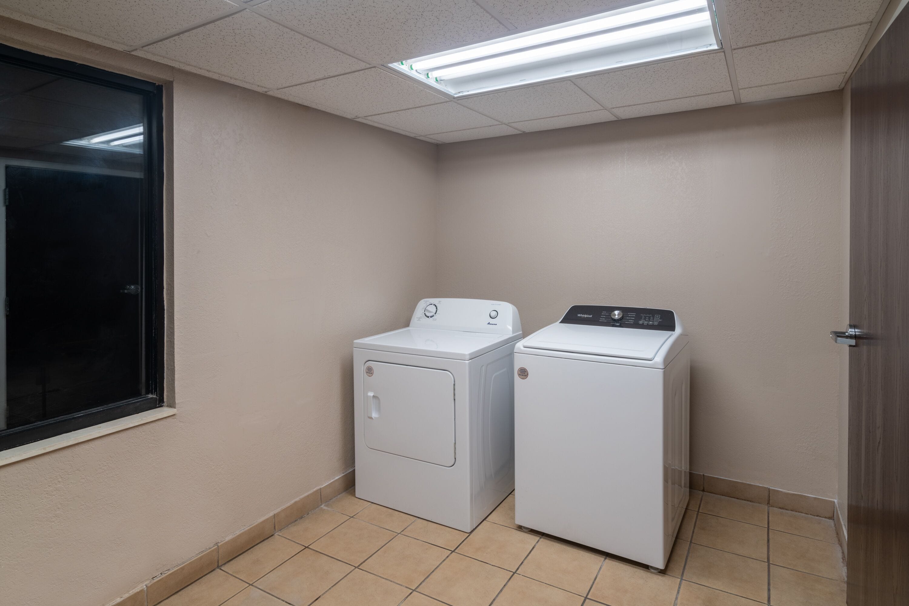 Uma lavanderia com duas máquinas de lavar brancas, uma janela e uma porta.