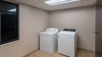 Uma lavanderia com duas máquinas de lavar brancas, uma janela e uma porta.