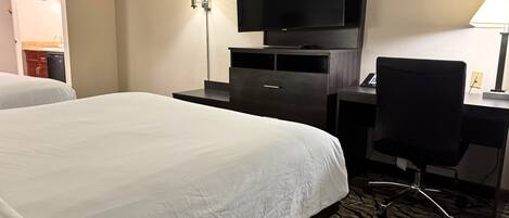 A hotel room with a large bed, a desk with a chair, a flat-screen TV, and a lamp.