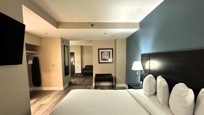A hotel room with a large bed, a desk with a lamp, a chair, a coat rack, and a television.