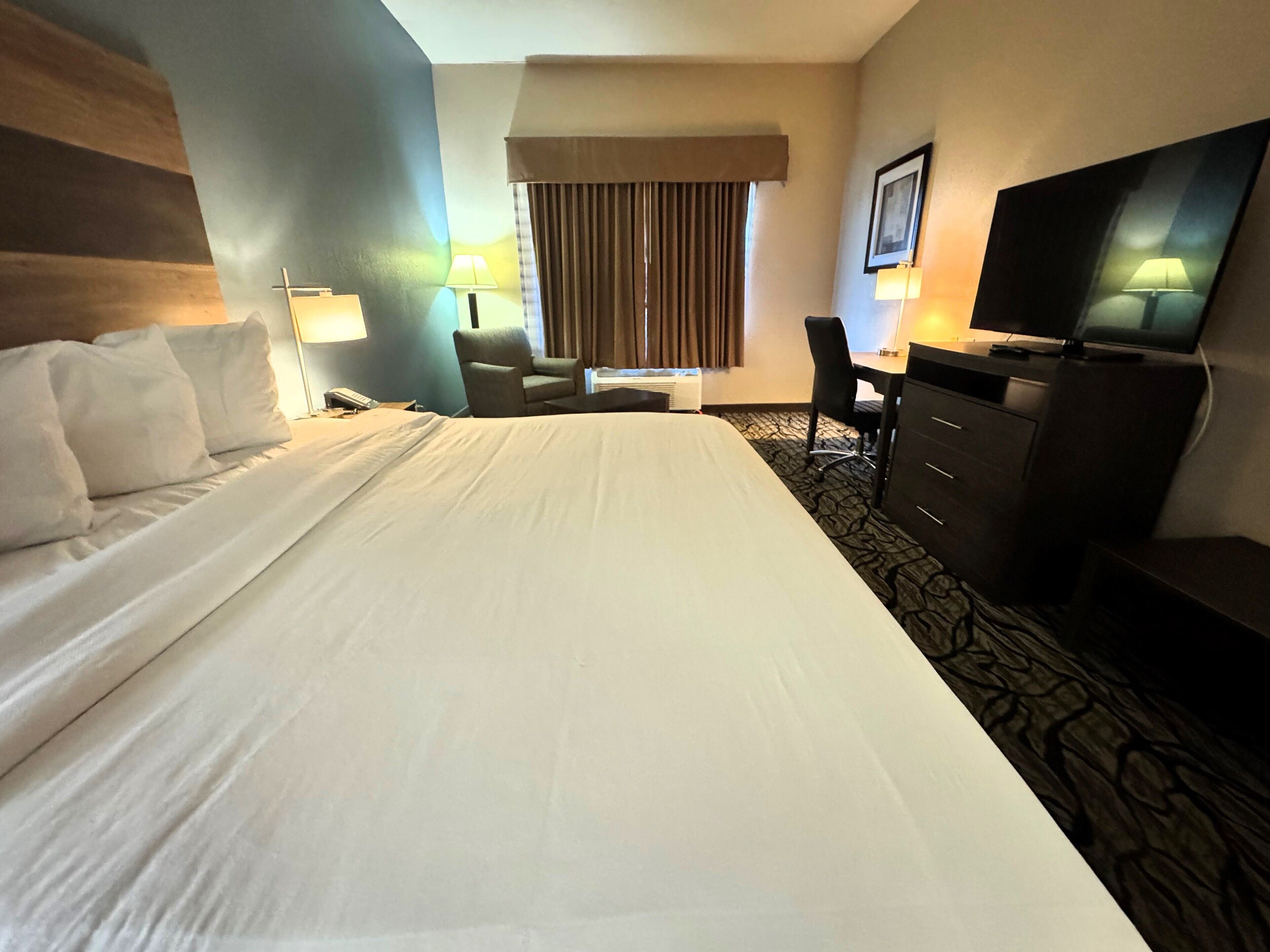 A hotel room with a large bed, a desk, a chair, a TV, and two lamps.