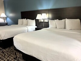 Habitación de hotel con dos camas, cada una con ropa blanca, cabeceros oscuros y dos lámparas de noche.