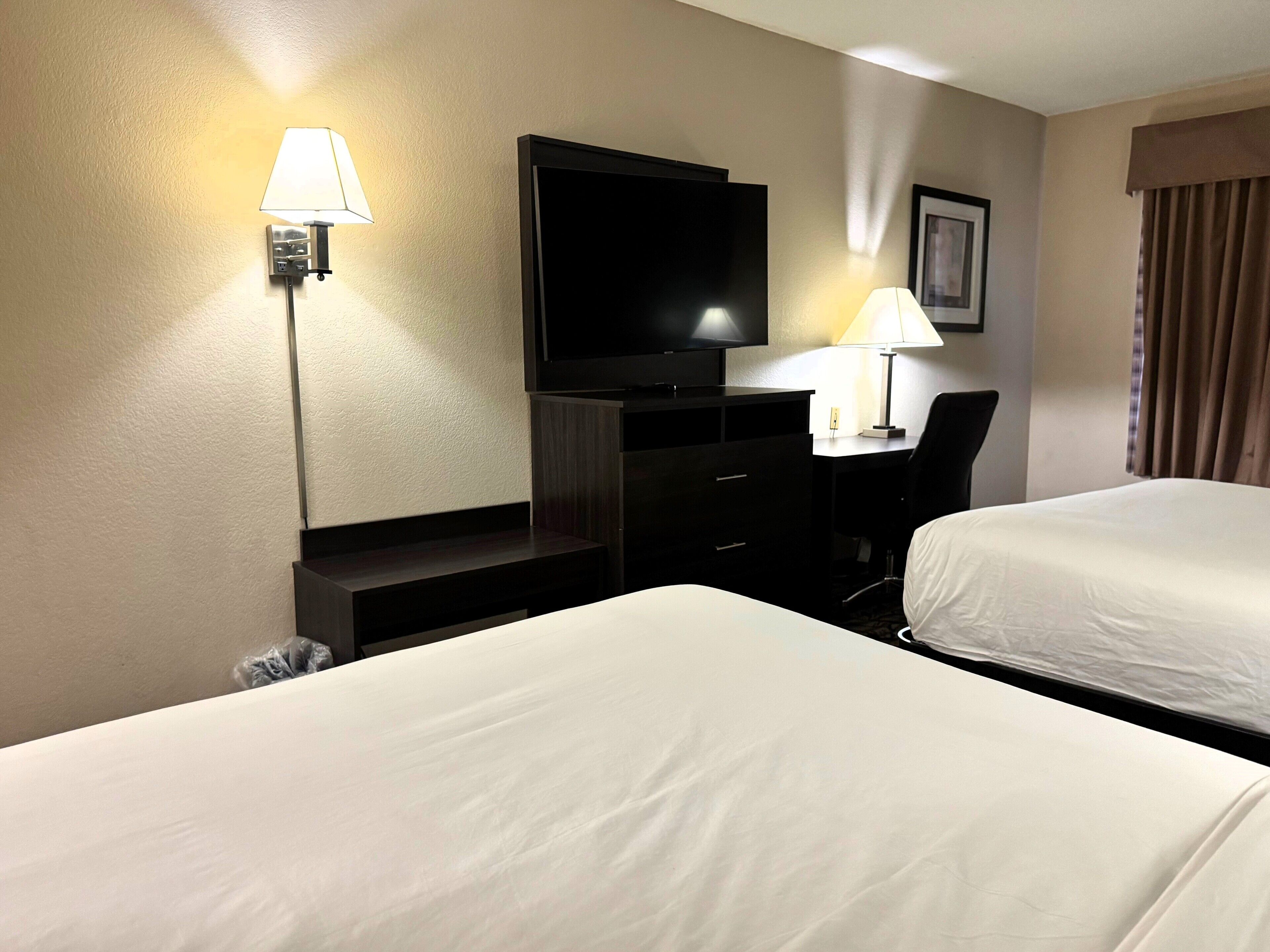 Una habitación de hotel con dos camas, un escritorio, un televisor y una lámpara.
