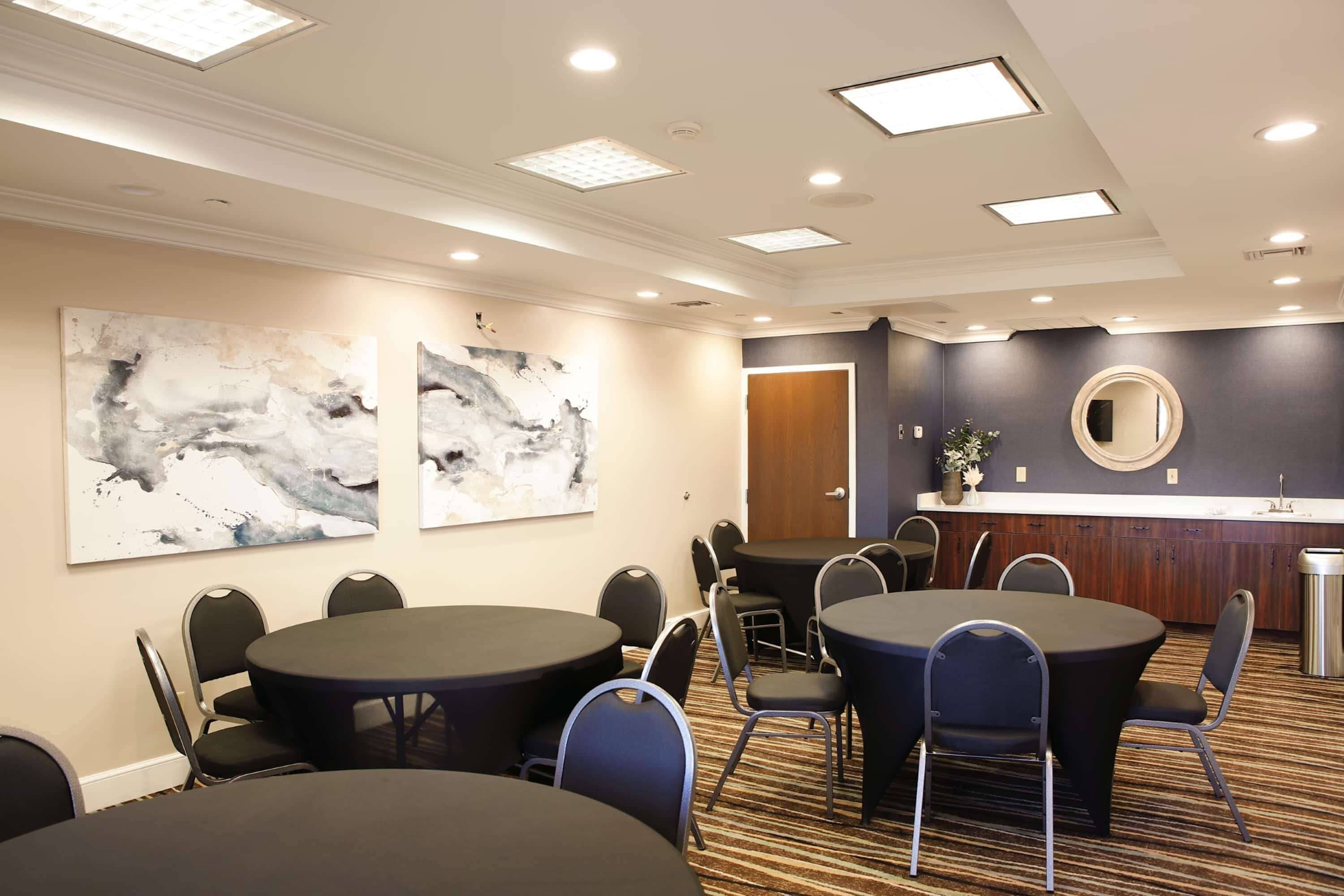 A conference room with round tables and chairs, a wooden counter with a mirror, and abstract wall art.