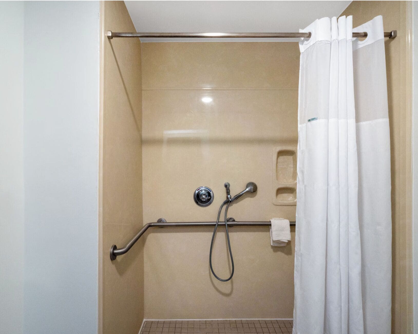 A shower area with a grab bar, a handheld showerhead, and a white curtain.