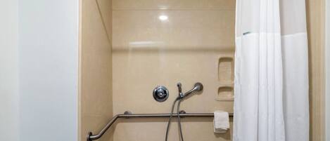 A shower area with a grab bar, a handheld showerhead, and a white curtain.