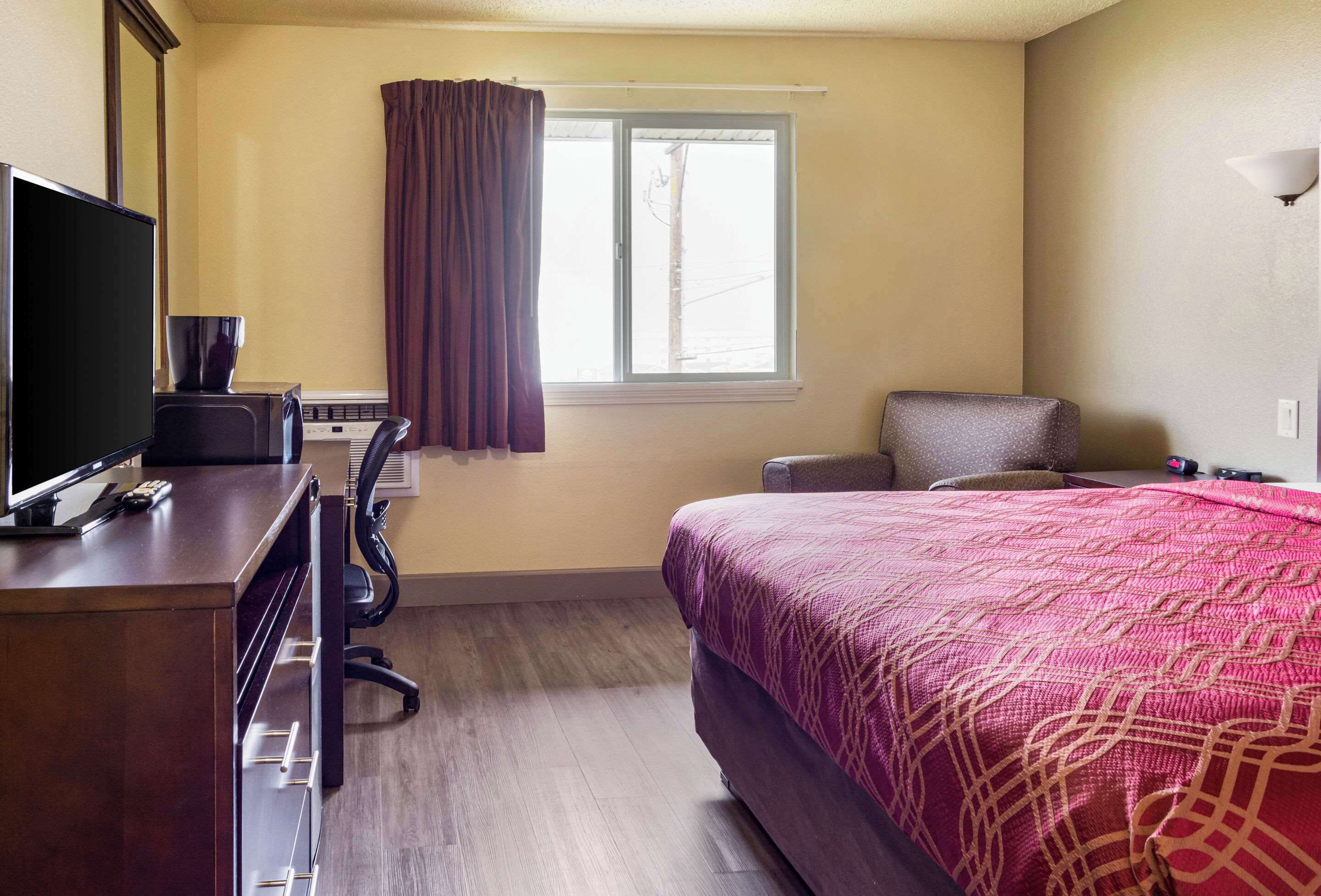 A hotel room with a bed, a desk with a computer, a chair, and a window with curtains.