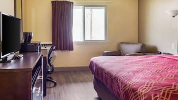 A hotel room with a bed, a desk with a computer, a chair, and a window with curtains.