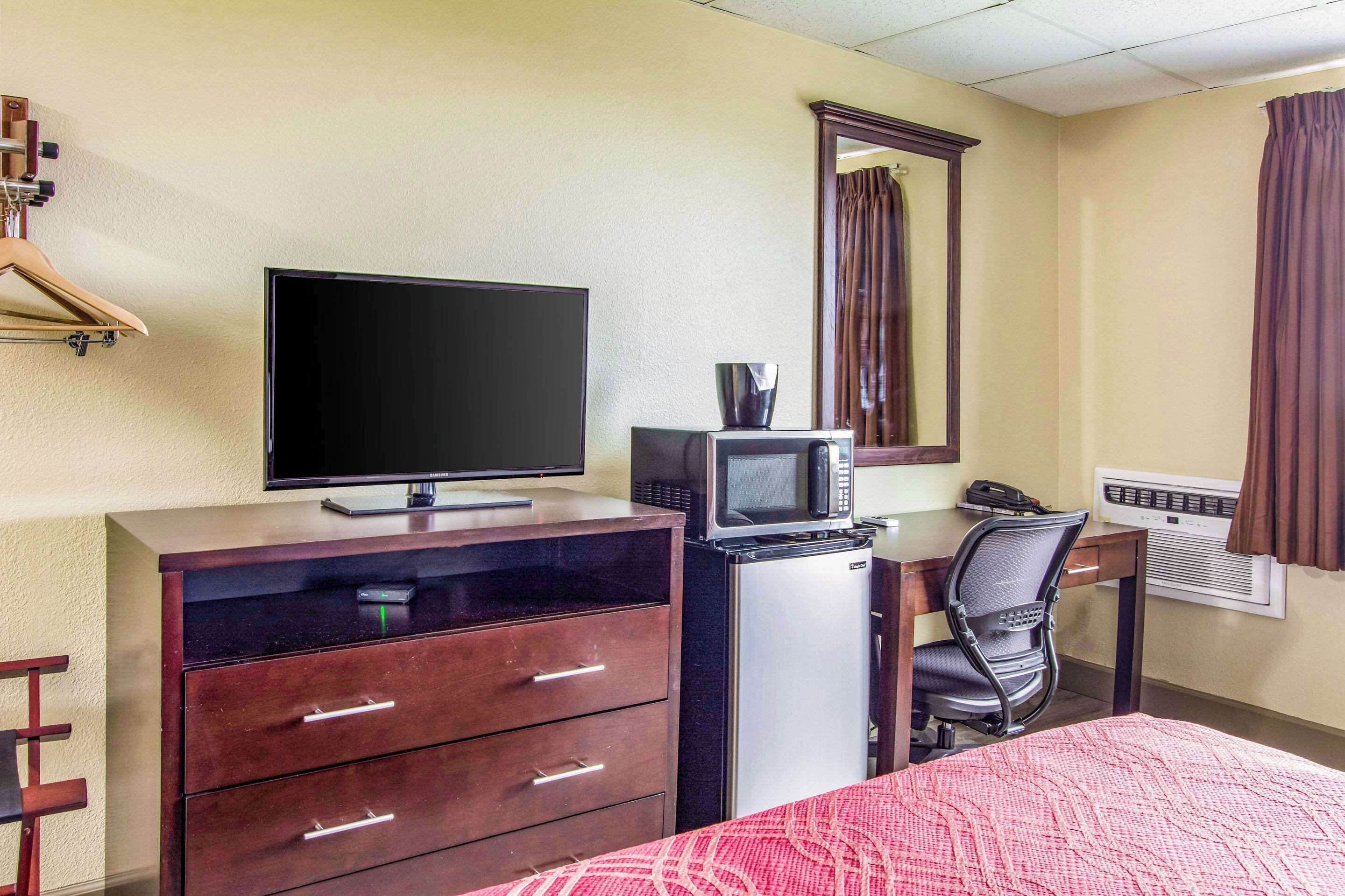 Une chambre d’hôtel comprenant un lit, une commode, un téléviseur, un four à micro-ondes, un bureau avec une chaise, un téléphone, un miroir et un appareil de climatisation.