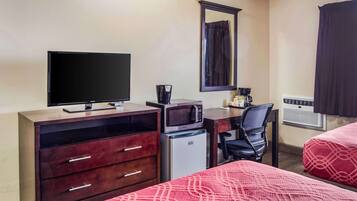 Une chambre d’hôtel équipée d’une télévision, d’un four à micro-ondes, d’un réfrigérateur, d’un bureau avec une chaise et de deux lits avec une literie rouge.