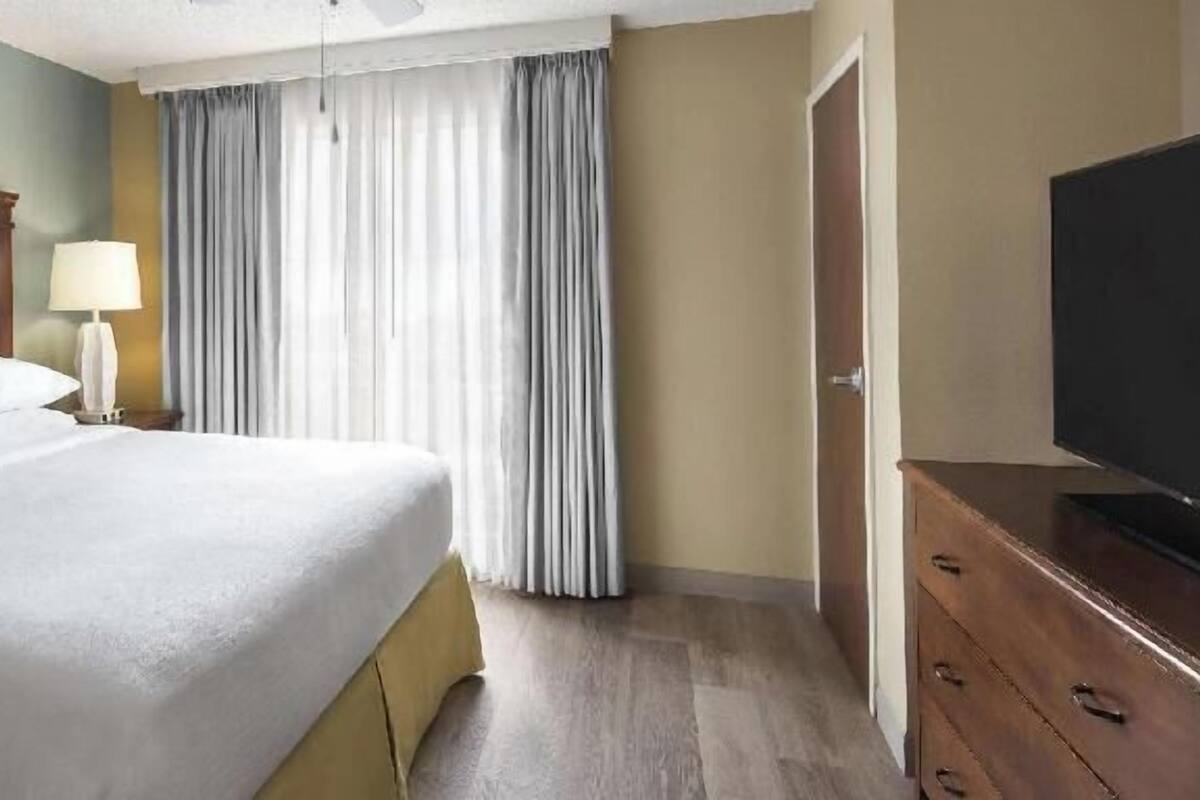 Ein Hotelzimmer mit Bett, Fernseher, Lampe und Vorhängen.