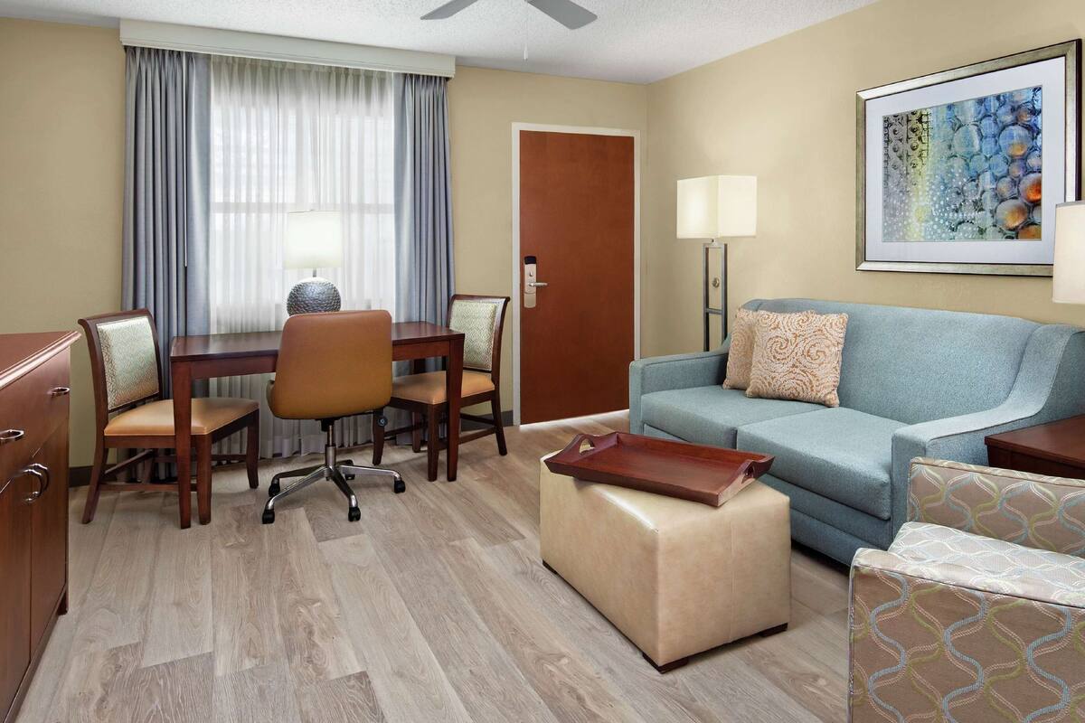 Une chambre d’hôtel équipée d’une télévision, d’une table à manger avec des chaises, d’un canapé, d’une causeuse et d’une lampe.