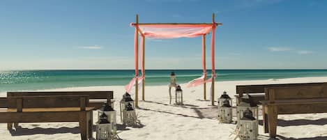 Une cérémonie célébrée sur la plage, avec une arche en bois, des bancs et des lanternes.