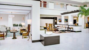 Eine großzügige Lobby mit mehreren Sitzbereichen, einem Empfangsbereich und einer Treppe, die verschiedene Ebenen miteinander verbindet.