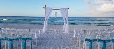 A beach wedding setup with white chairs and a canopy.